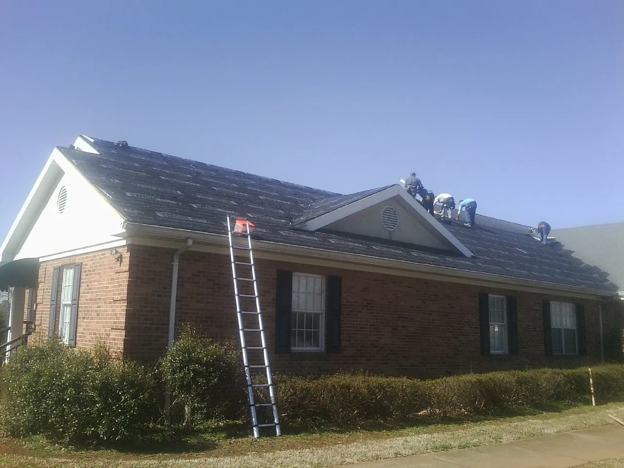 Crew tearing shingles off a brick ranch roof with a ladder set — Metal Roof Repair work by our crew in Claysville