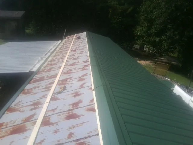 Old rusted panels beside newly installed green metal roofing — Wind Damage Roof Repair by Roofing Brothers in Claysville