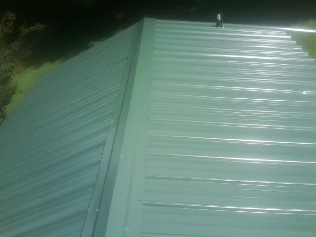 New green metal panels meeting at the ridge of a roof — Flat Roof Repair work by our crew in Claysville