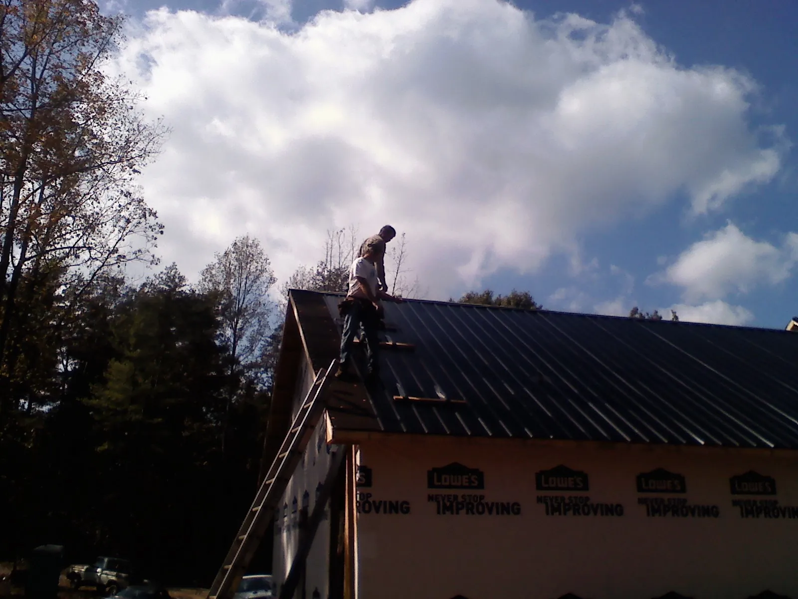 Roofer fastening dark metal panels high against a cloudy sky, from a Roof Inspection job in Claysville