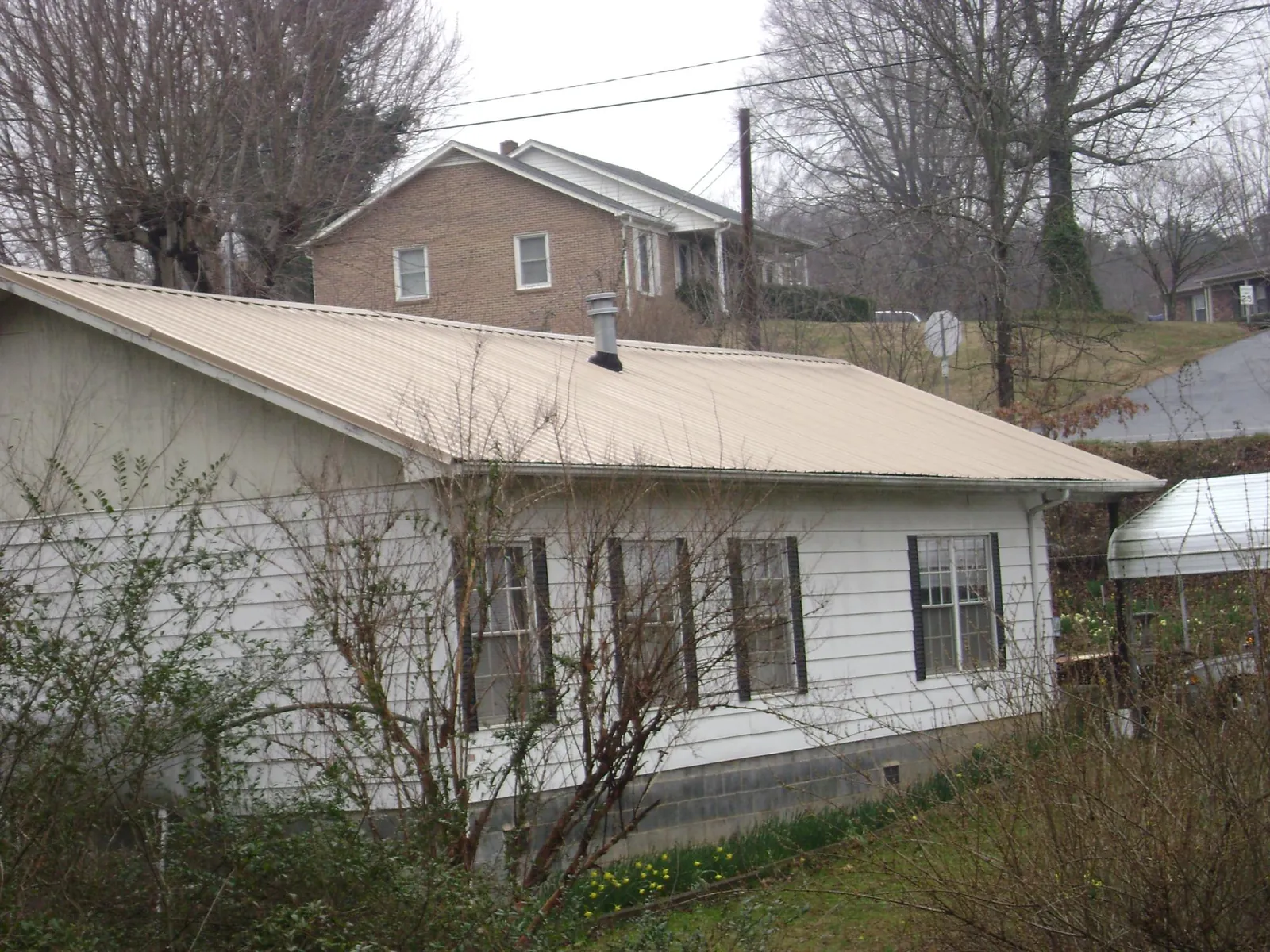 Tan metal roof on a white sided house set into a hillside — Commercial Roofing by Roofing Brothers in Claysville